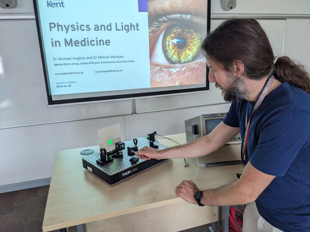 Man adjusting a Michelson interferometer, in front of a screen saying 'Physics and Light in Medicine'