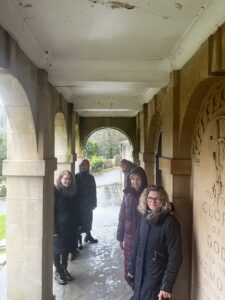 Image shows a group of women smiling and looking at the camera. They are stood in two lines, in a small open corridor.