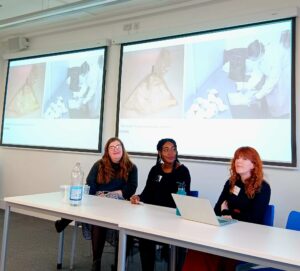 Image shows Harriet Jackson, Gabrielle Bryan-Quamina and Sarah Bond sitting at a table in a row. Behind, there is a screen showing various objects.