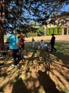 A group of people standing in a garden. Two are sitting on a bench.