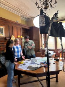 A group of people standing around a table, underneath filming equipment.