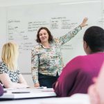 Instructor pointing to white board with students looking