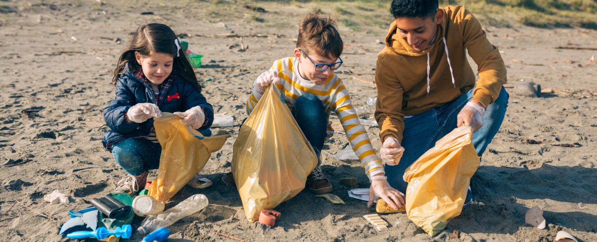 Three children collecting litter from a sandy beach